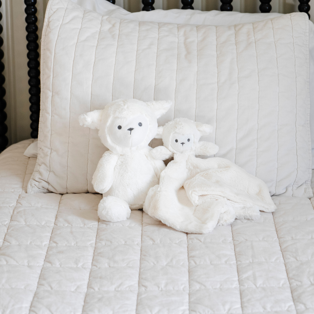 A white lamb stuffed animal and lovey from Saranoni on a bed.
