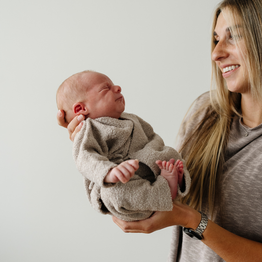 Mom holds newborn baby boy wearing taupe bamboni lite outfit.