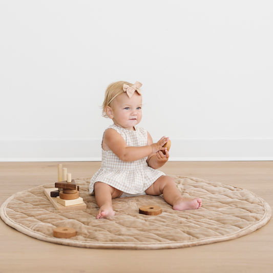 Baby girl sits on a hazelnut minky play mat and is playing with some toys.