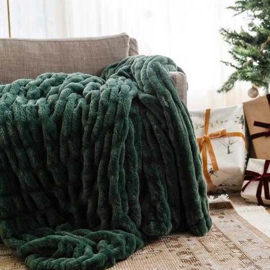 Plush green double ruched blanket draped over a sofa beside a Christmas tree and presents, creating a cozy, festive atmosphere in the living room. Ideal for holiday home decor and winter warmth. The soft blanket is a luxury blanket and a Saranoni blanket.