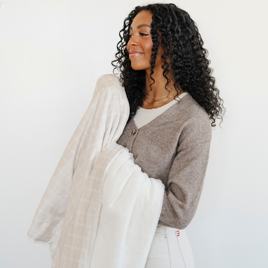 A woman smiles and holds a luxuriously soft Saranoni minky/lush blanket. This premium dual-textured throw features Saranoni’s signature cream lush fabric on one side and ultra-soft square printed minky on the other. Designed for ultimate relaxation, this plush blanket is perfect for snuggling, movie nights, and adding a touch of luxury to any home. This soft blanket is a luxury blanket and a Saranoni blanket. The cozy blanket is a perfect comfort item and a comfortable blanket.