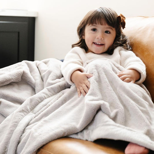A little girl is wrapped in a Luxury Toddler Feather (light gray) Colored Lush Saranoni Blanket. The soft blanket is a baby blanket or toddler blanket.