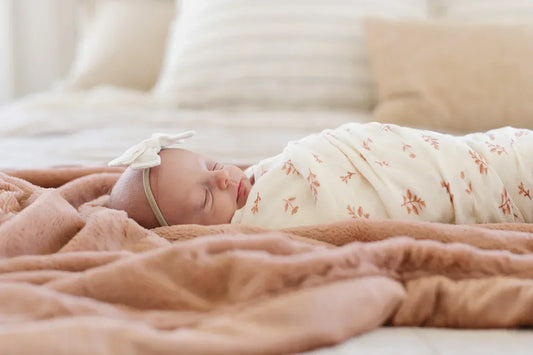 A newborn swaddled in a Saranoni blanket with a delicate floral print, cradled in an adult's arms on a soft, neutral bed.