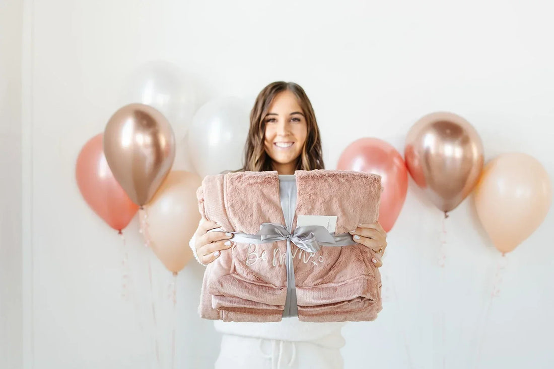A woman in a soft striped dress holds a Saranoni throw, embodying the warmth of a gift chosen for her.