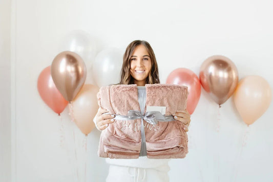 A woman in a soft striped dress holds a Saranoni throw, embodying the warmth of a gift chosen for her.