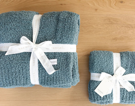 Two folded teal Saranoni blankets, one large and one small, tied with white ribbon