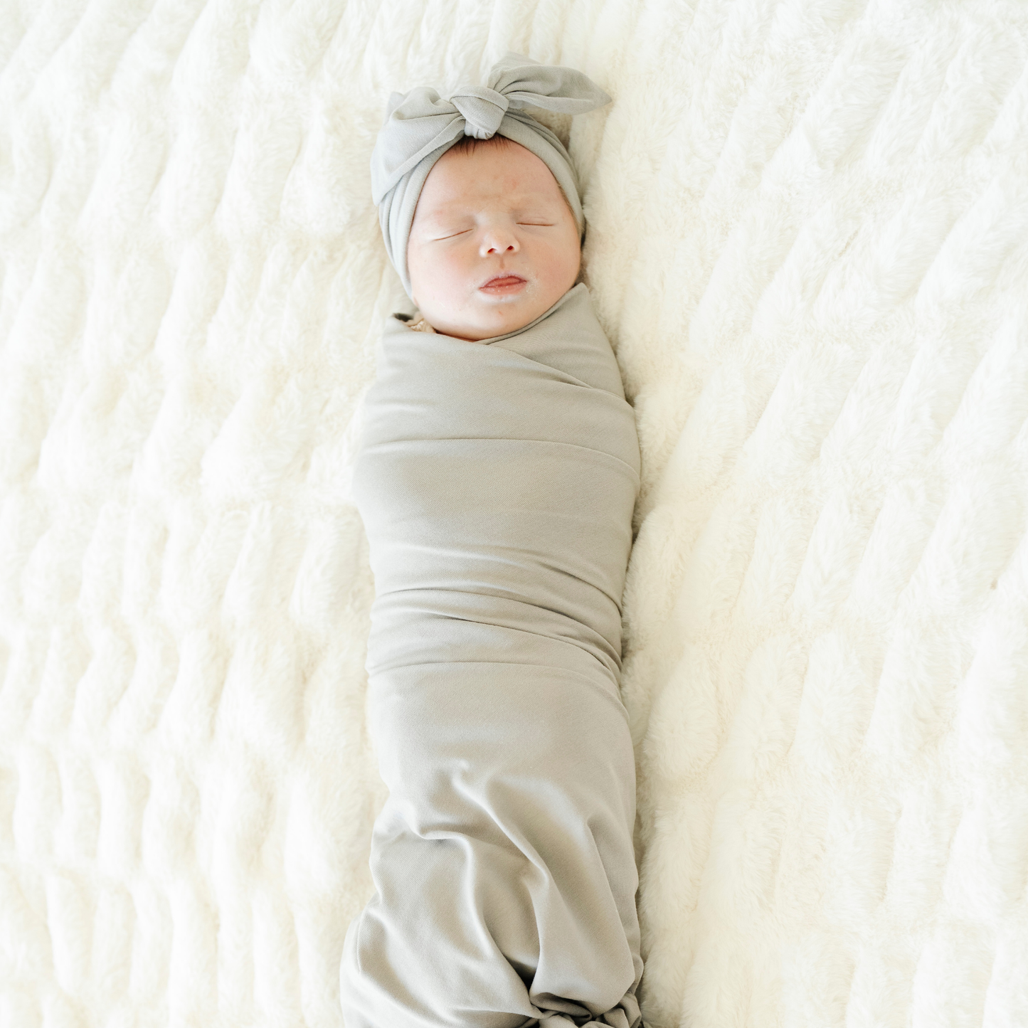 Baby girl swaddled in Ash Saranoni Stretchy Swaddle with a matching bow. 