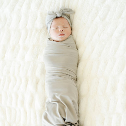 Baby girl swaddled in Ash Saranoni Stretchy Swaddle with a matching bow. 