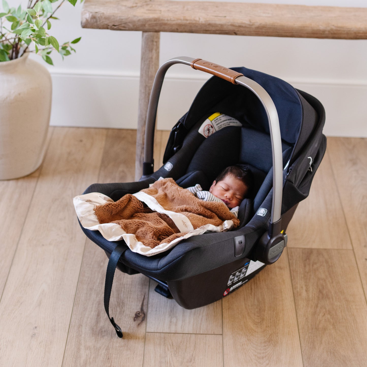 Baby sleeping in car seat with a cozy and soft tan satin border blanket. 