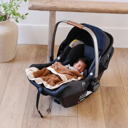 Baby sleeping in car seat with a cozy and soft tan satin border blanket. 