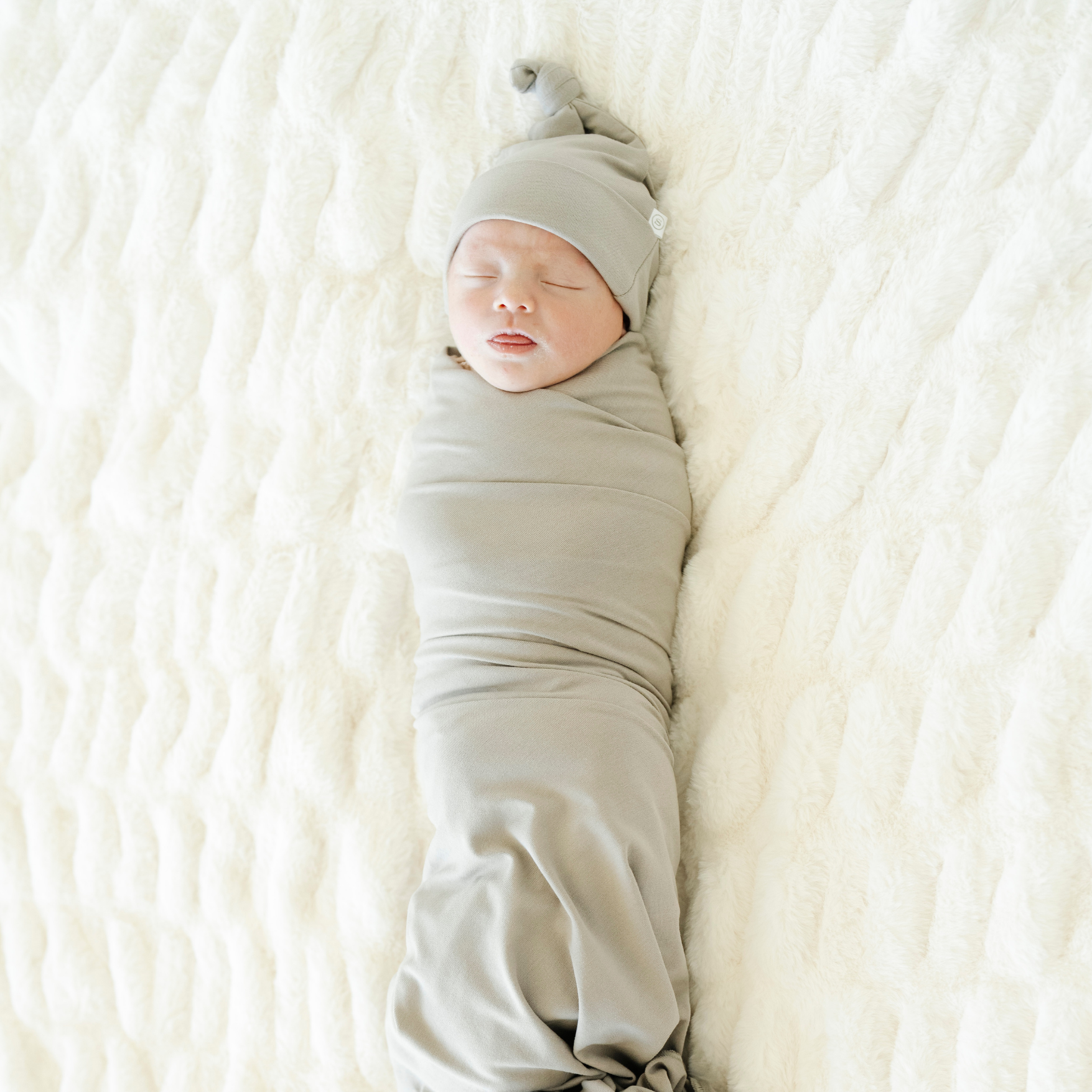Baby girl swaddled in Saranoni soft Stretch swaddle in Ash color with a matching hat. 