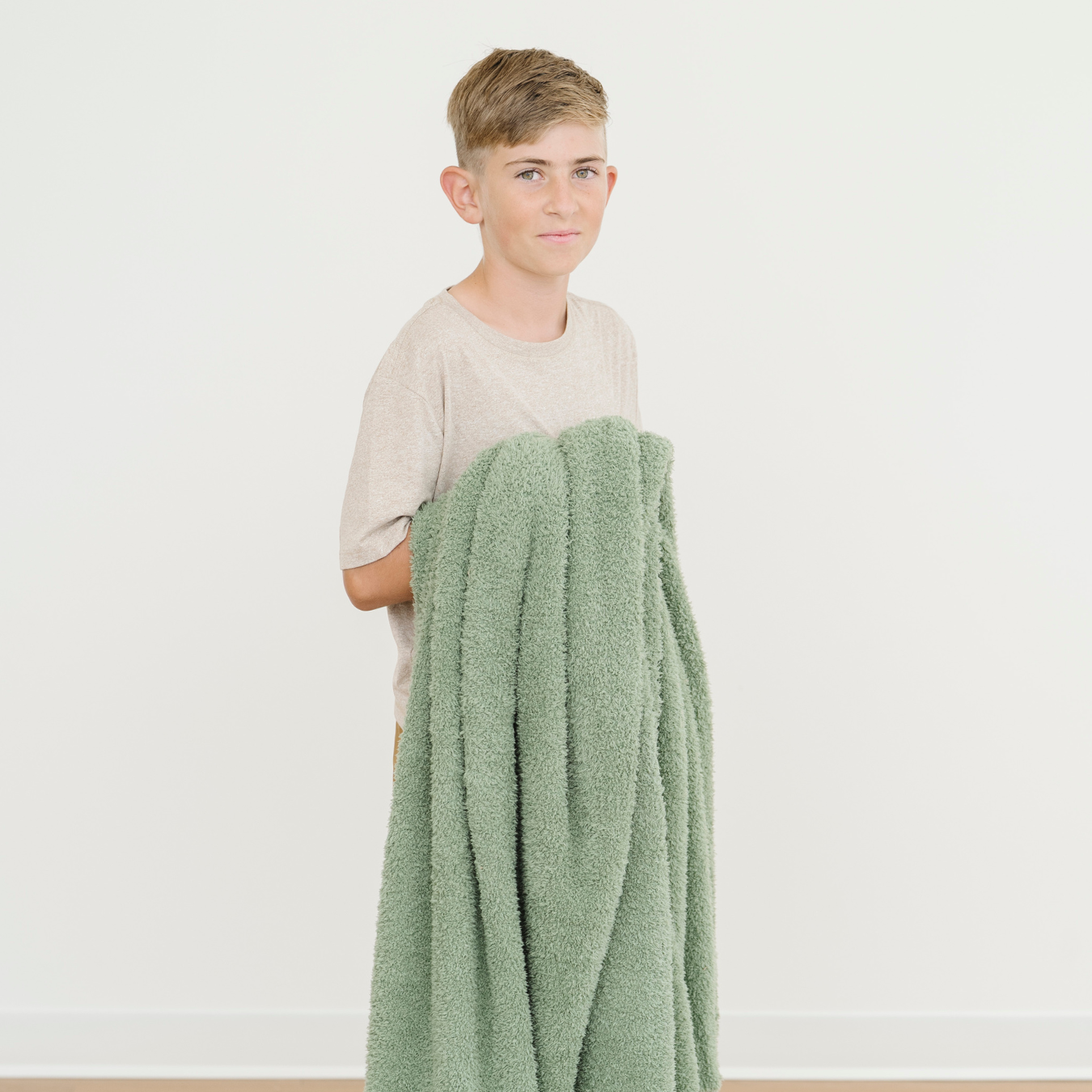 Boy holding an olive green bamboni blanket.