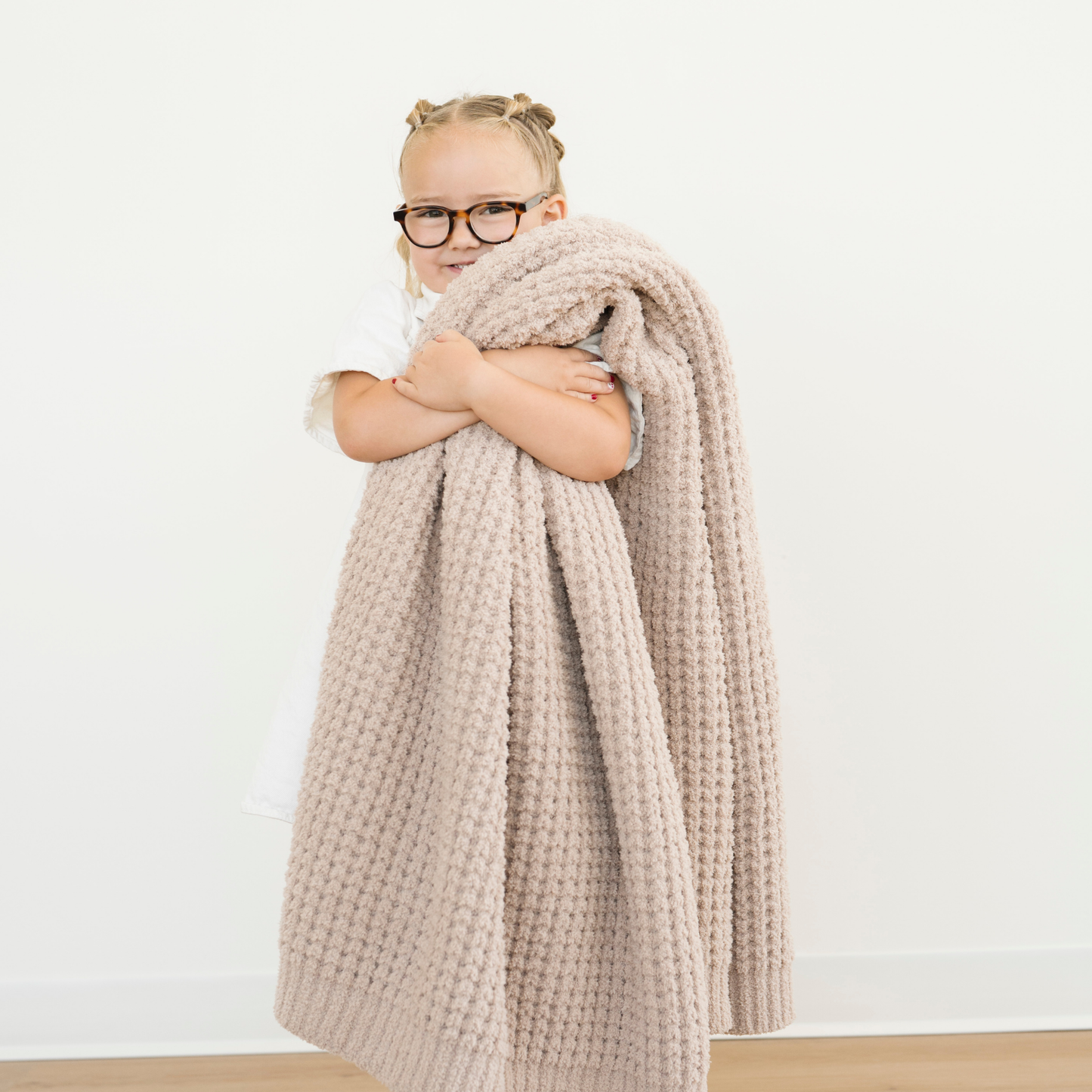 Girl snuggles a soft Waffle Knit Toddler Blanket in Wheat tan color. 