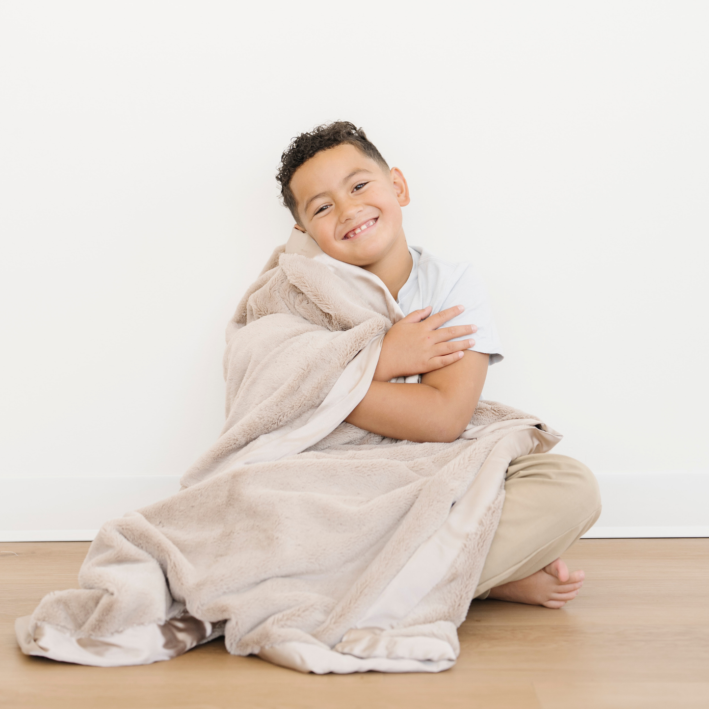 Boy snuggled with Saranoni Tan Satin Lush Border Toddler large blanket. 