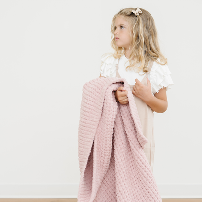 Little girl holds a soft waffle knit toddler blanket that is pink.