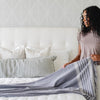 Woman with curly hair making a bed with a gray striped blanket - Saranoni
