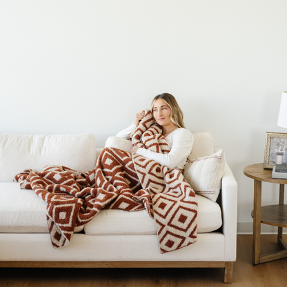 Woman snuggled on couch with Khmer Double Layer Bamboni Throw soft blanket.
