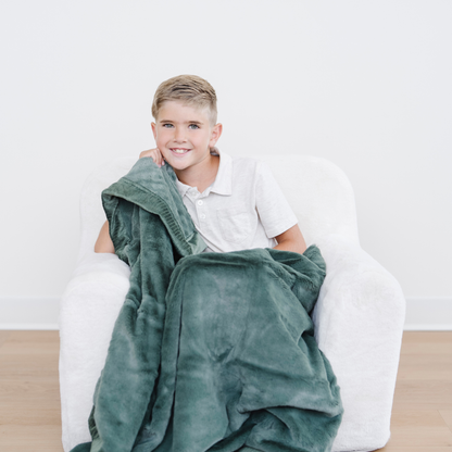 Boy snuggled with hunter green lush toddler blanket in a chair. 