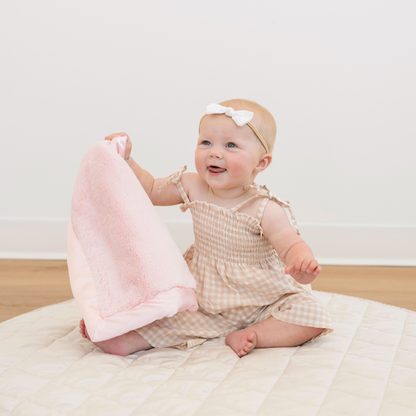 Baby girl holding Light Pink Satin border mini baby blanket. 