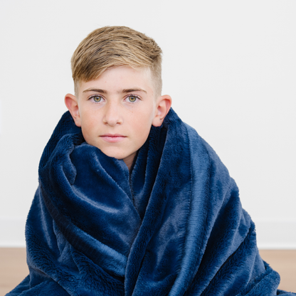 Boy wrapped in lush navy blue toddler blanket. 