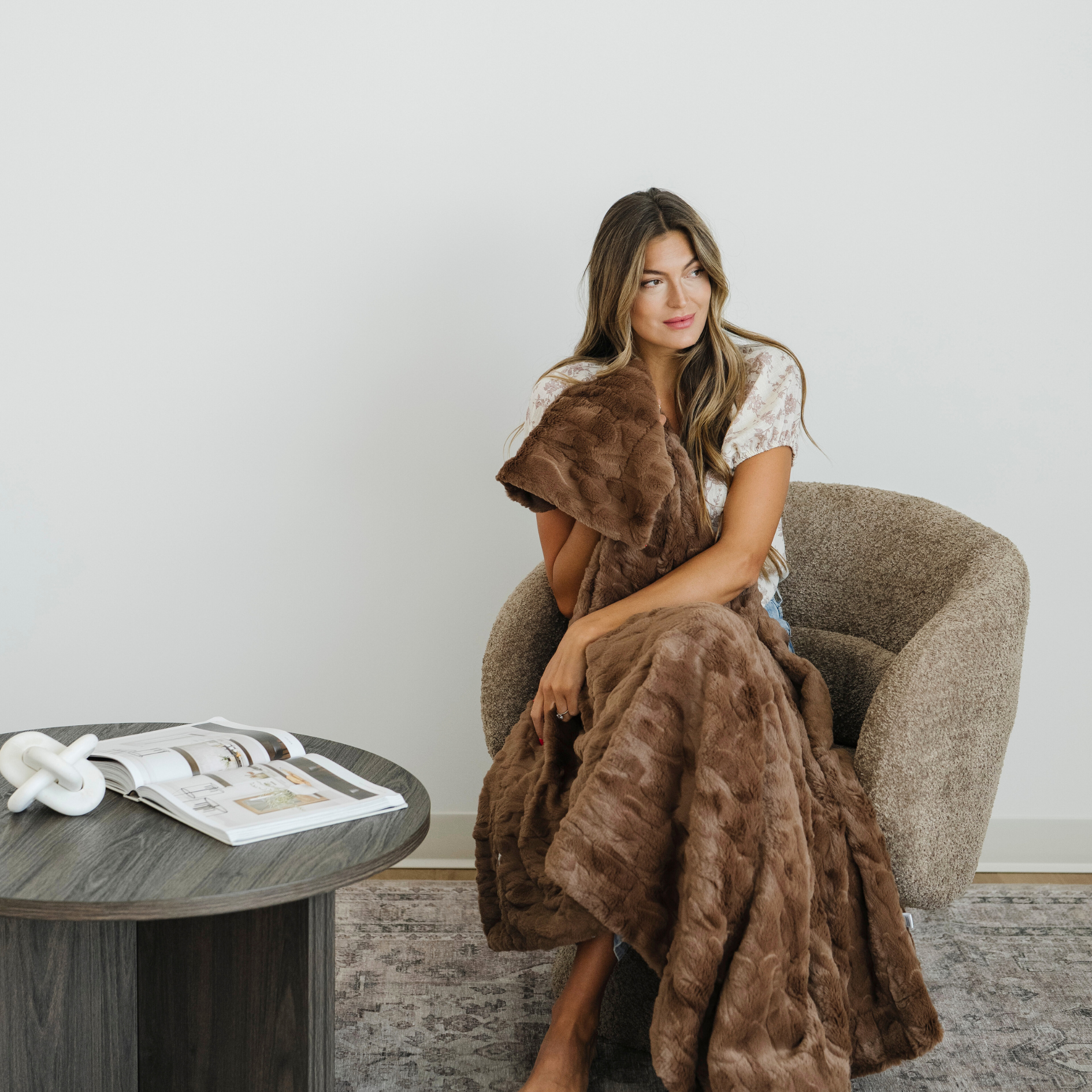 Woman sitting in chair wrapped in a brown patterned faux fur throw blanket. 