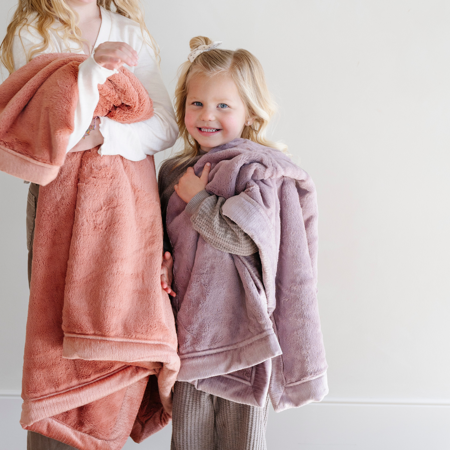 A little girl holds a Luxury Receiving Bloom (dusty purple) Colored Lush Saranoni Blanket. The soft blanket is a small blanket and a baby blanket or toddler blanket.
