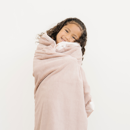 Young girl snuggled with Lush toddler blanket with a satin border in a light pink Daisy print. 