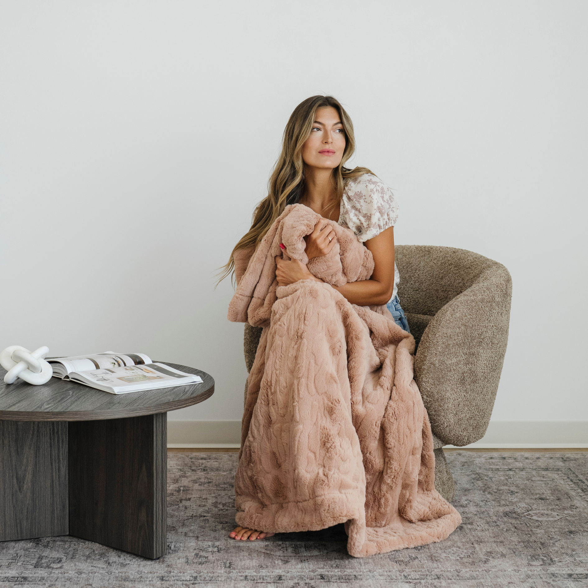 Woman sitting in a chair with a pink faux fur cozy blanket draped over her. 