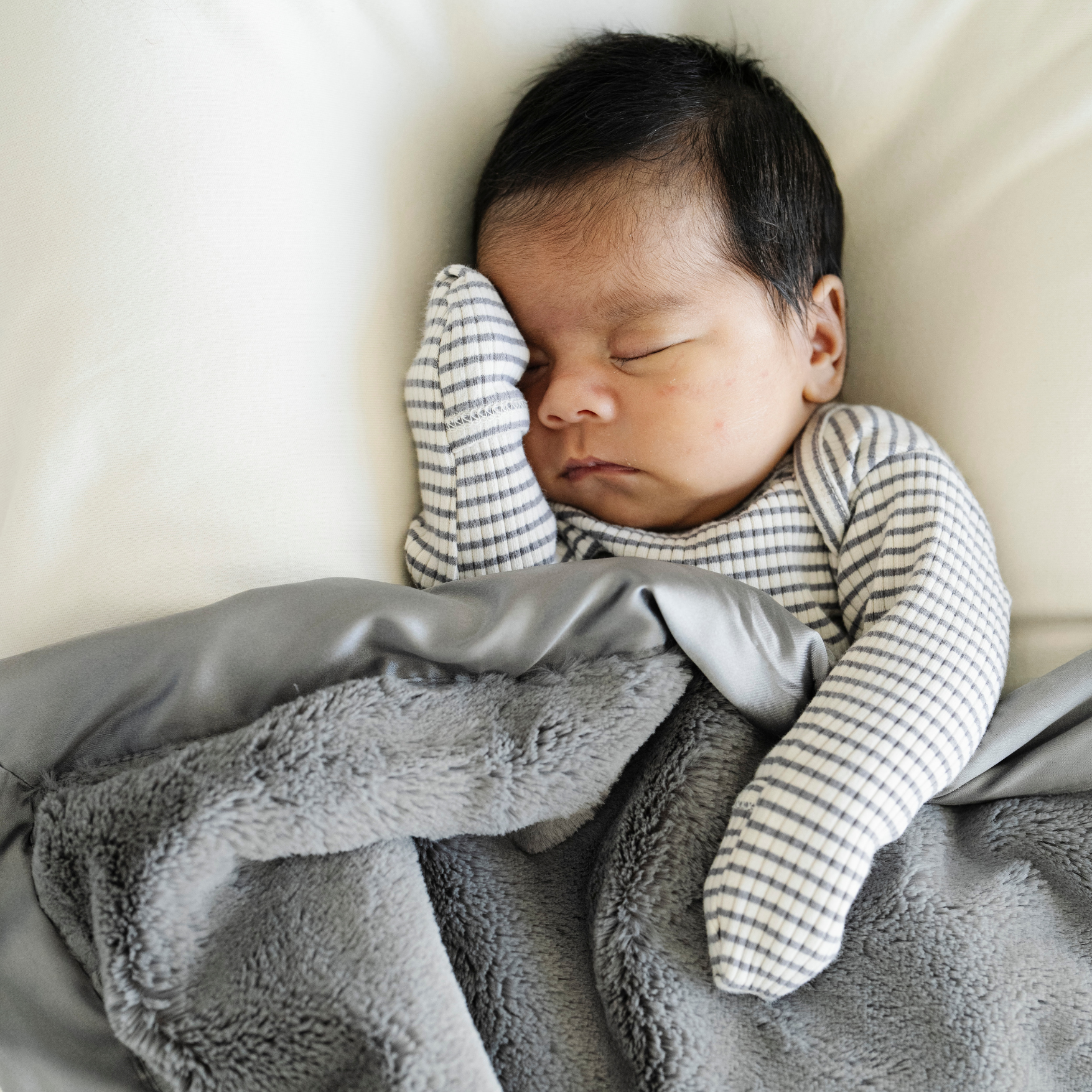 Baby boy snuggled in Saranoni satin border mini blanket in Gray. 