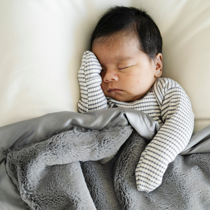 Baby boy snuggled in Saranoni satin border mini blanket in Gray. 