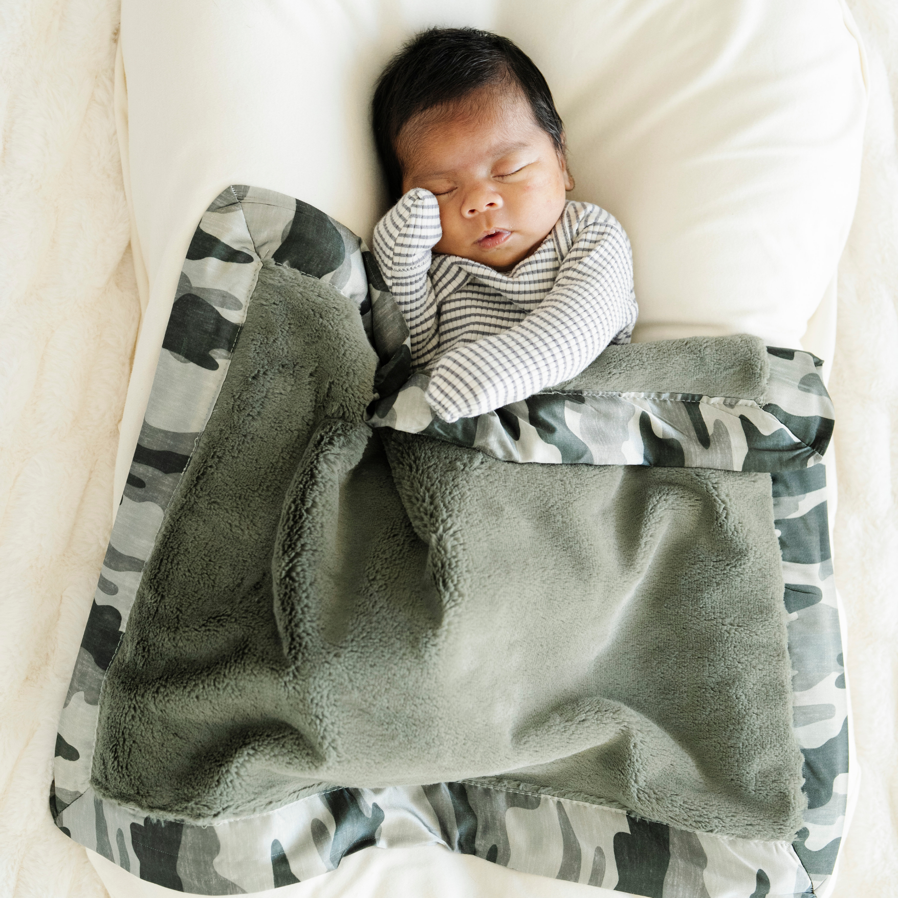 Baby boy snuggled in Saranoni satin border mini baby blanket in Camo print. 