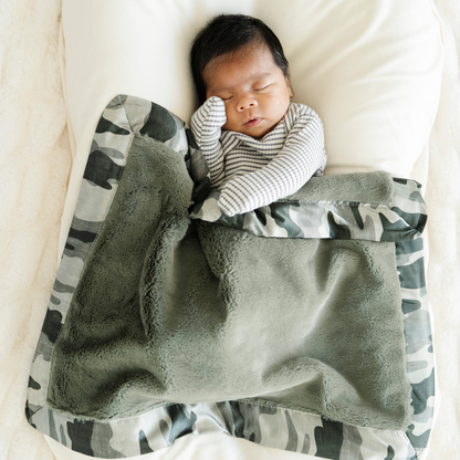 Baby boy snuggled in Saranoni satin border mini baby blanket in Camo print. 