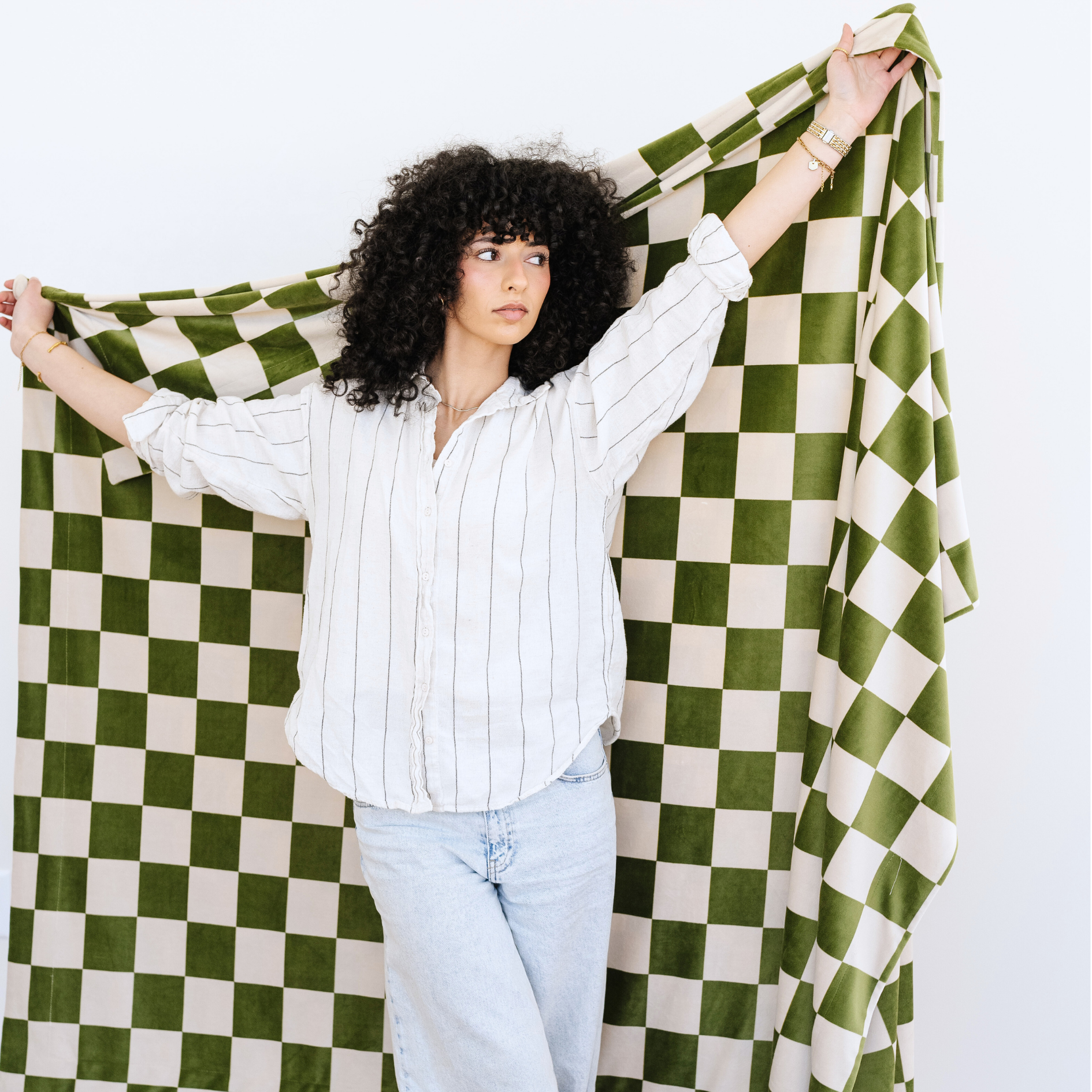 Woman stands holding a Olive and Cream checkered minky stretch XL blanket. 