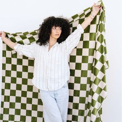 Woman stands holding a Olive and Cream checkered minky stretch XL blanket. 