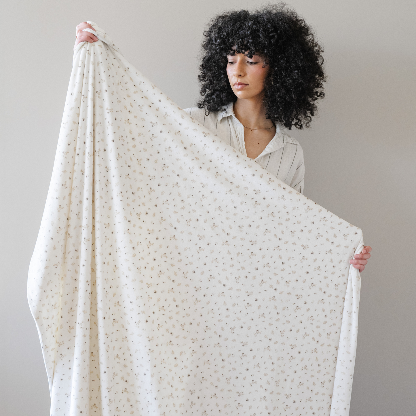 Woman stands holding a floral minky stretch blanket with a warm neutral floral print on it. 