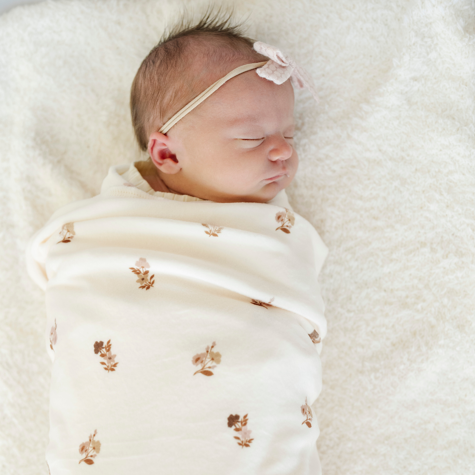 A newborn baby girl is swaddled in a baby blanket that has a floral pattern on it. 
