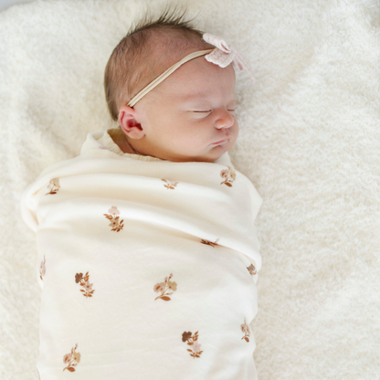 A newborn baby girl is swaddled in a baby blanket that has a floral pattern on it. 