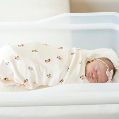 A newborn baby girl is swaddled in a floral blanket that is a minky stretch luxe swaddle. 
