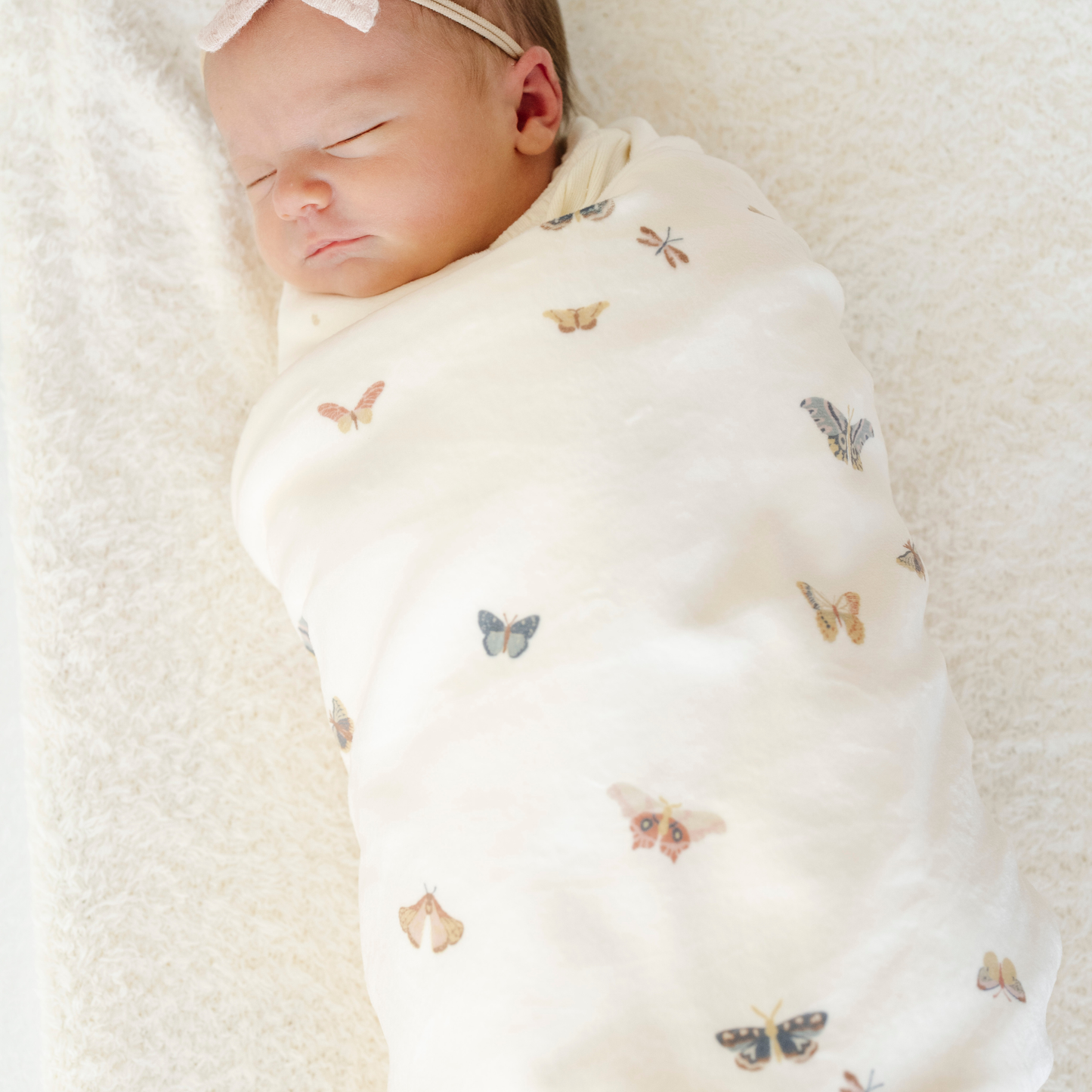 A newborn baby girl is swaddled in a minky stretch luxe blanket that has butterflies on it. 