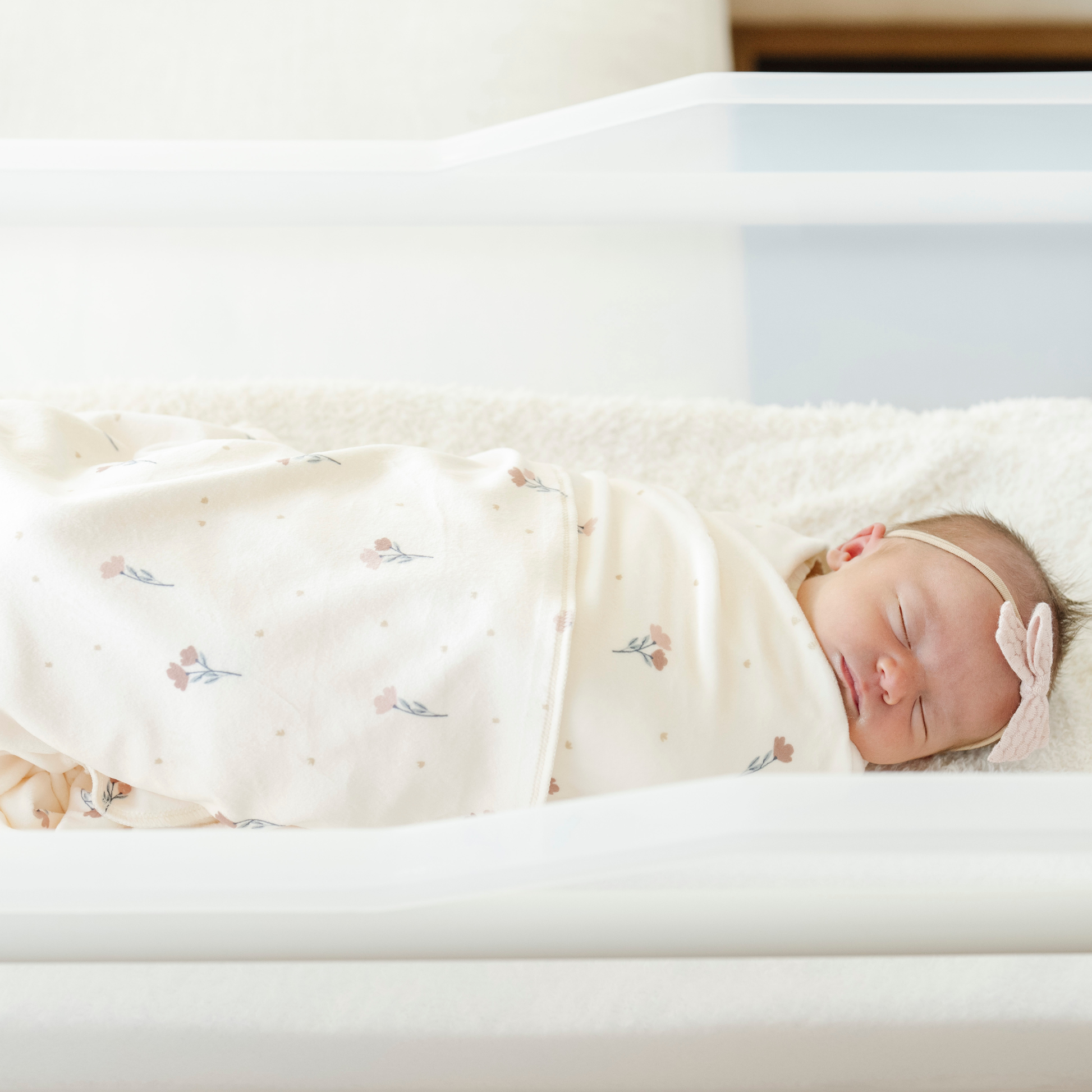 A newborn baby girl is swaddled in a floral minky stretch luxe swaddle. 