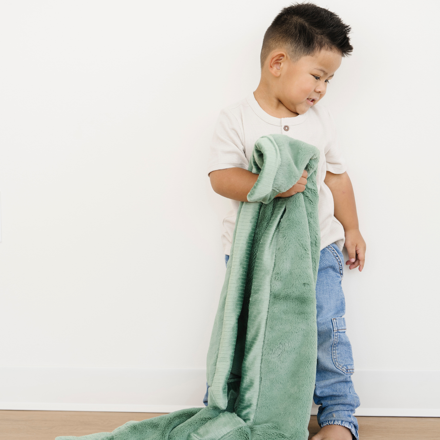 Toddler boy snuggles a lush toddler blanket in a Seagrass green color. 