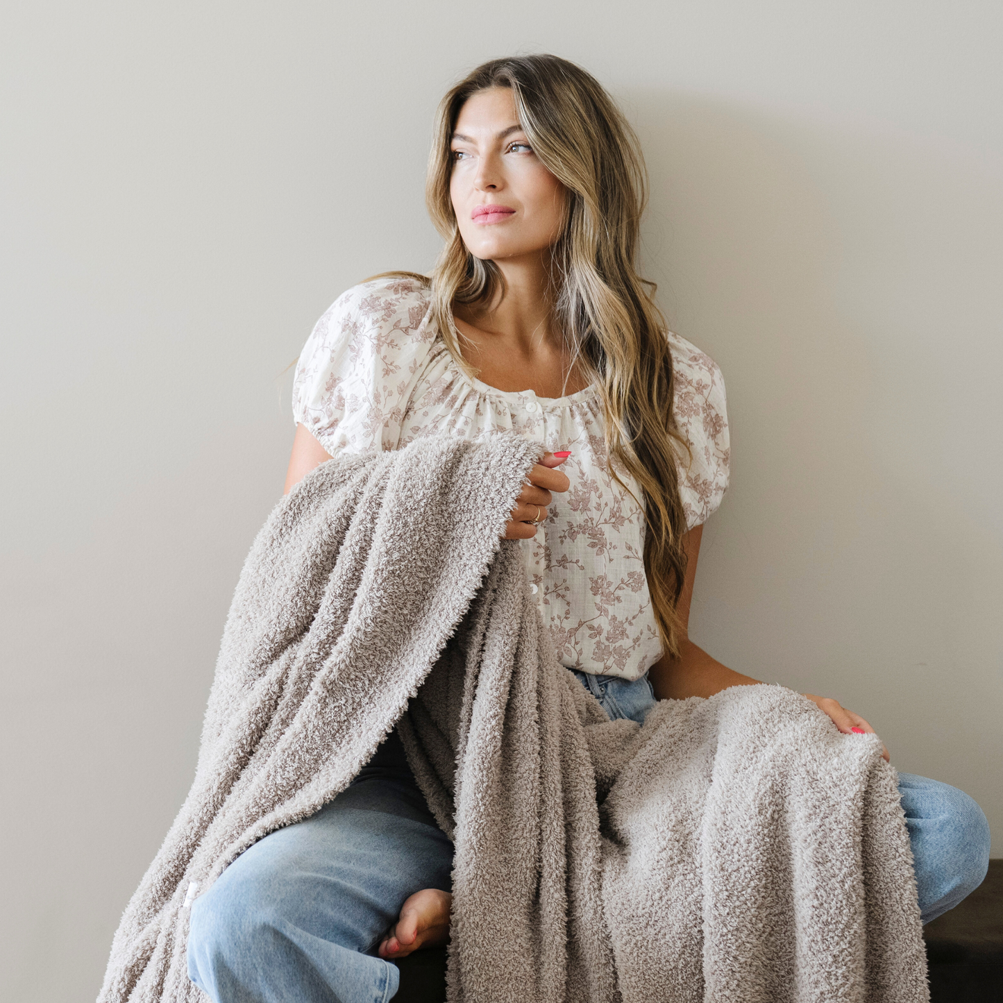Woman sits snuggled with taupe bamboni extra large blanket. 