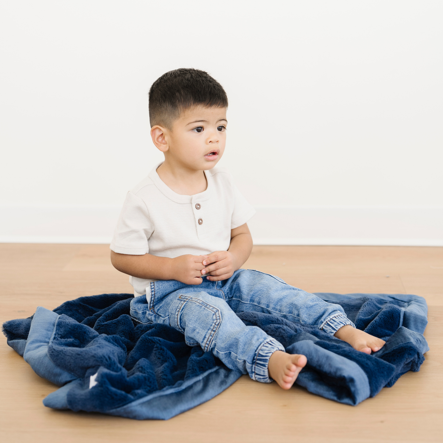 Toddler boy sitting on Lush Receiving baby blanket in Navy blue color. 