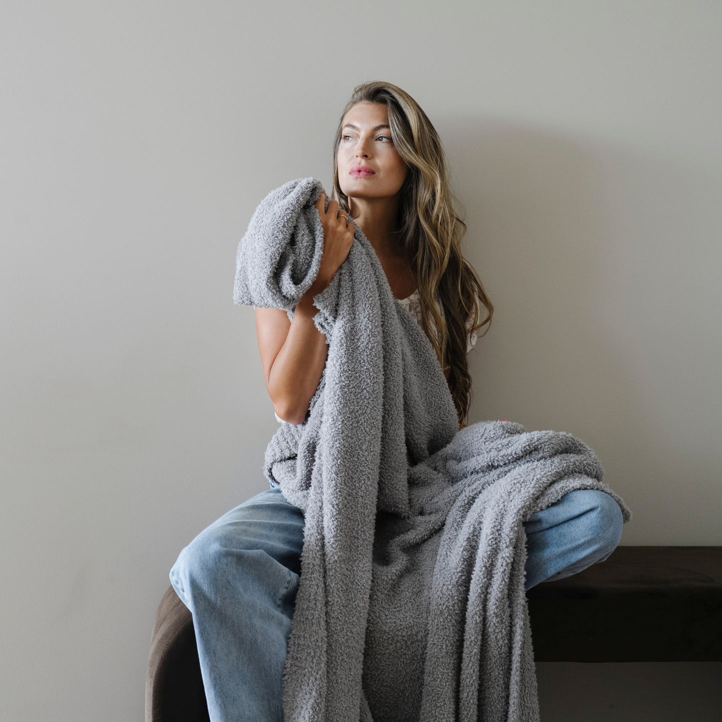 Woman sits wrapped in gray bamboni extra large cozy blanket.
