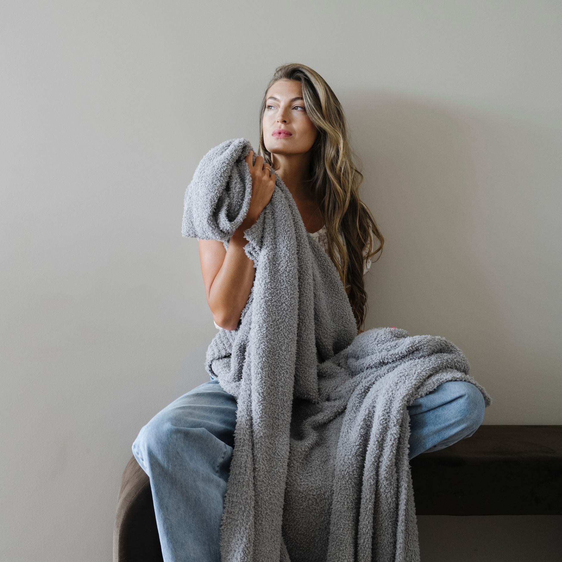 Woman sits wrapped in gray bamboni extra large cozy blanket.