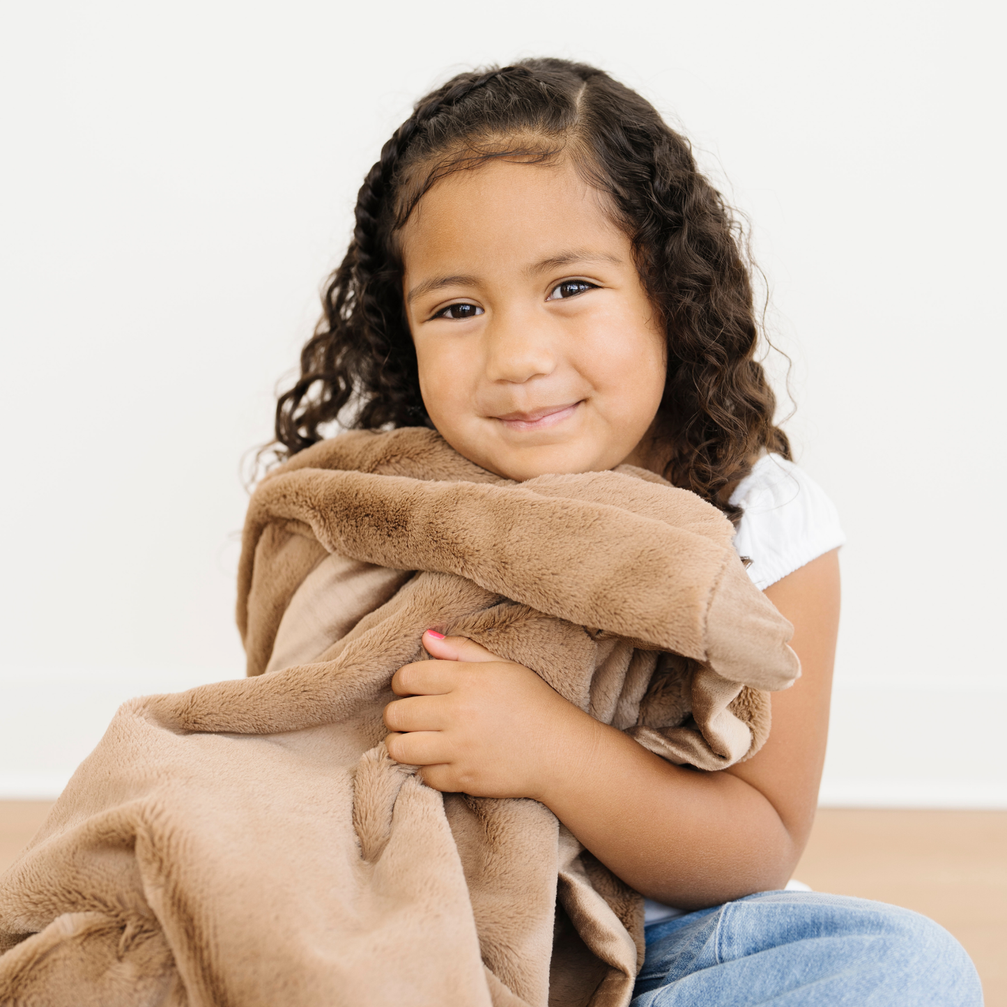 Girl snuggled in a Lush Toddler Saranoni Blanket in Hazelnut. 