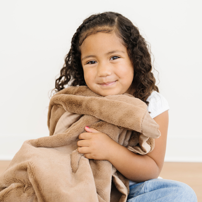 Girl snuggled in a Lush Toddler Saranoni Blanket in Hazelnut. 
