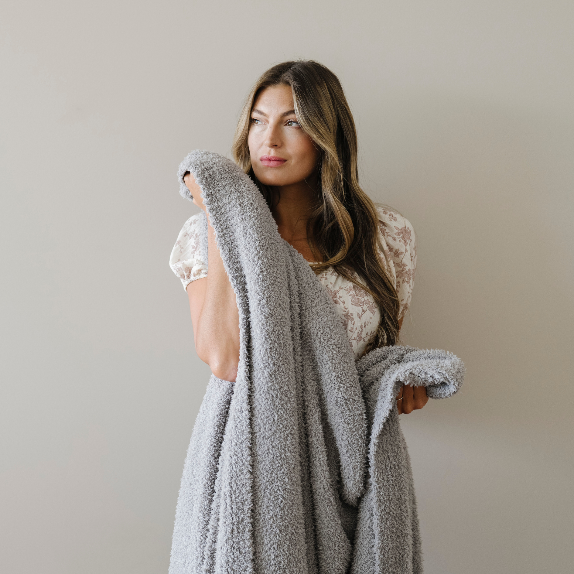 Woman stands snuggled with a gray bamboni extra large cozy blanket.