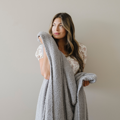Woman stands snuggled with a gray bamboni extra large cozy blanket.