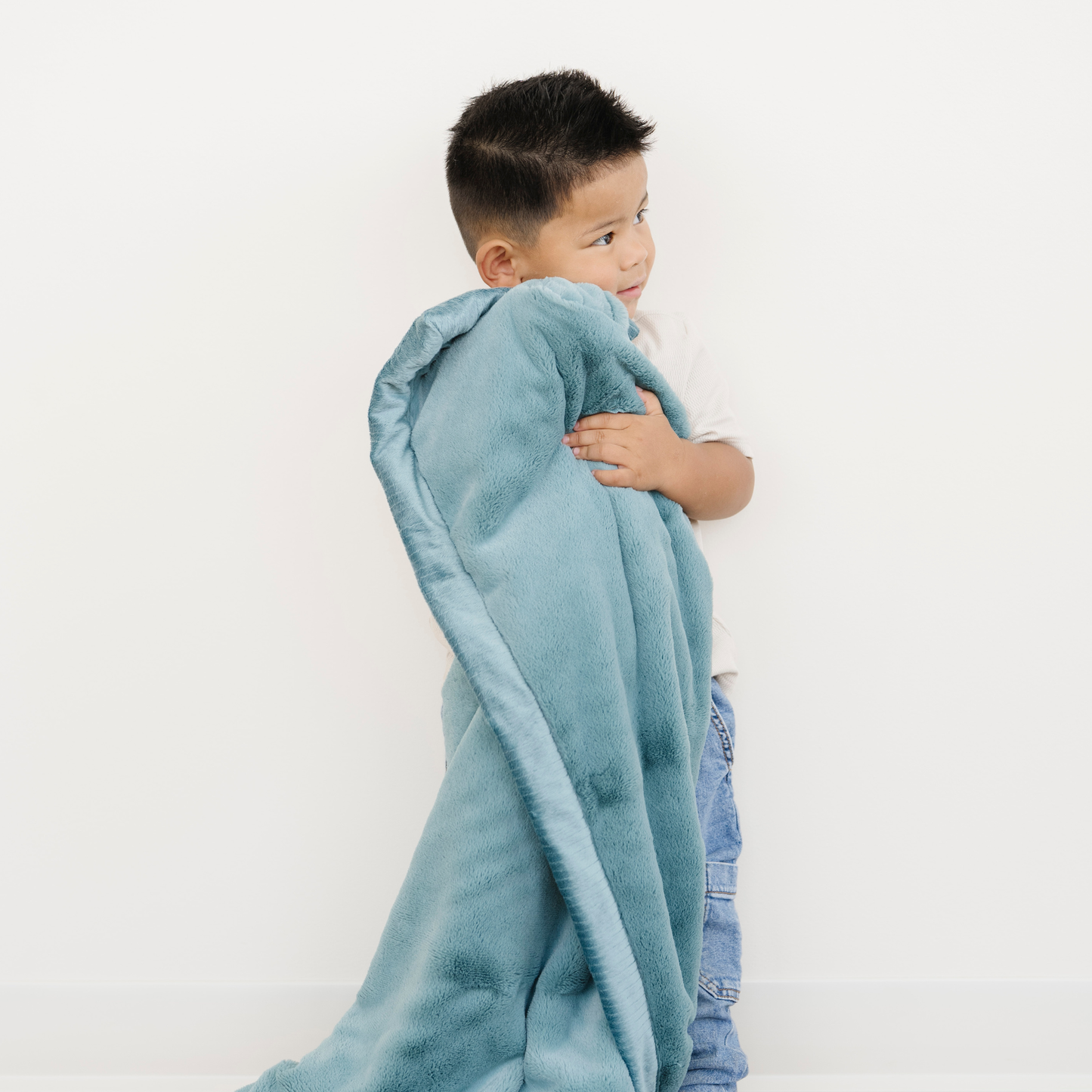 Toddler boy snuggled with Saranoni Lush Toddler Blanket in Mineral Blue. 